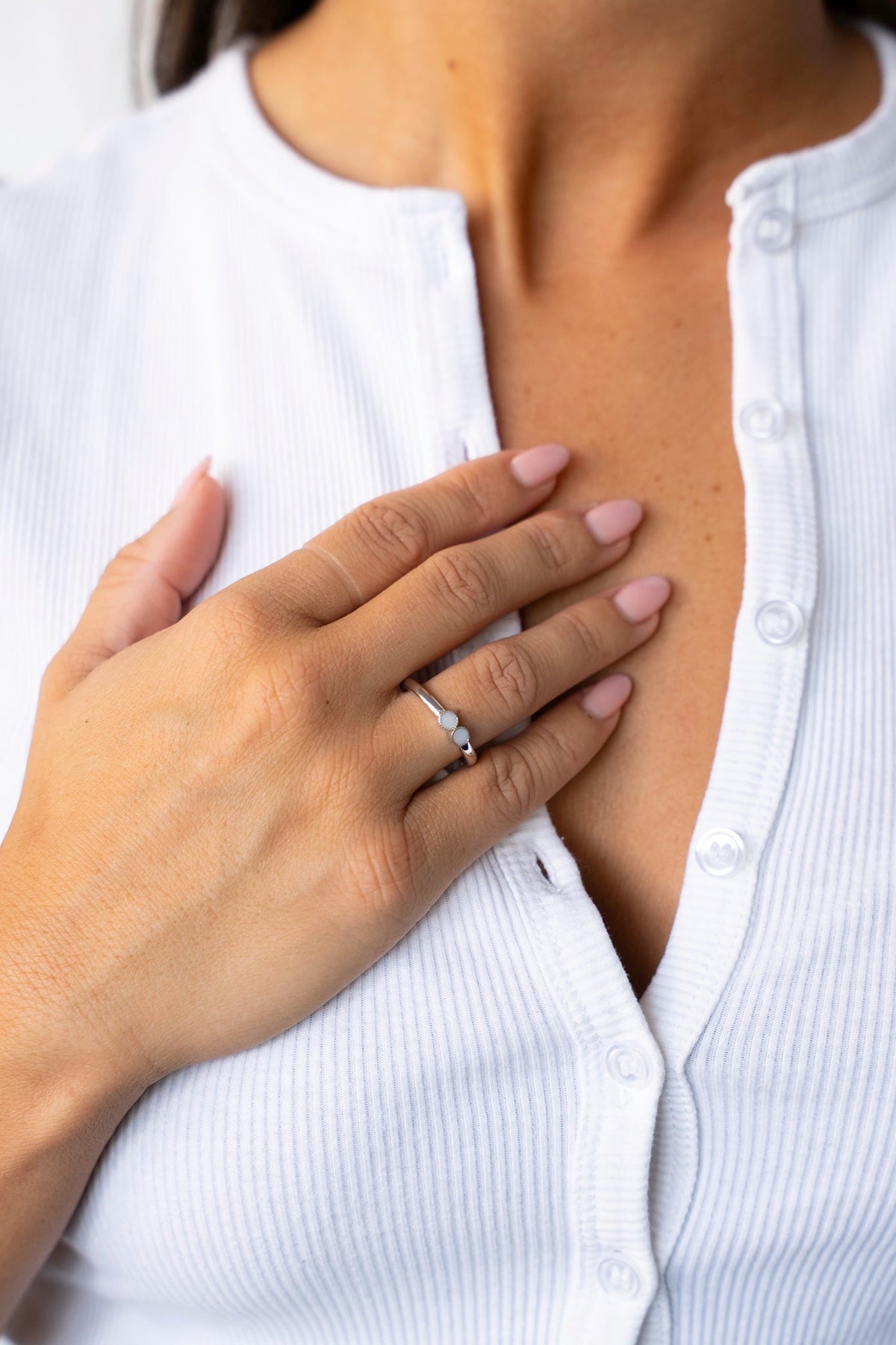 Vrouw in een wit geribd vest legt haar hand op de borst, met de Bo-ring van massief witgoud.