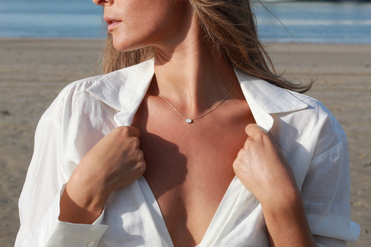 Hanger van massief witgoud met een ronde moedermelkhars in het midden, gedragen door een vrouw met een open blouse.