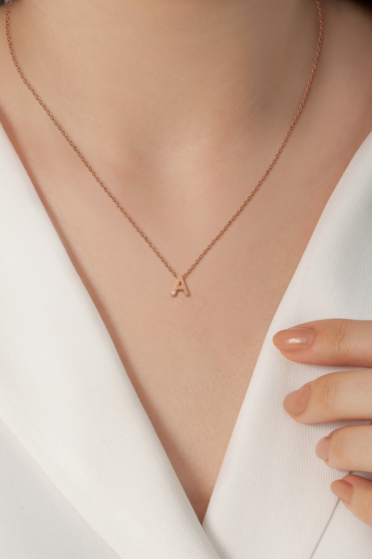 Roségouden hanger met een letter 'A' en een kleine steen van moedermelk, gedragen door een persoon in een witte blouse.