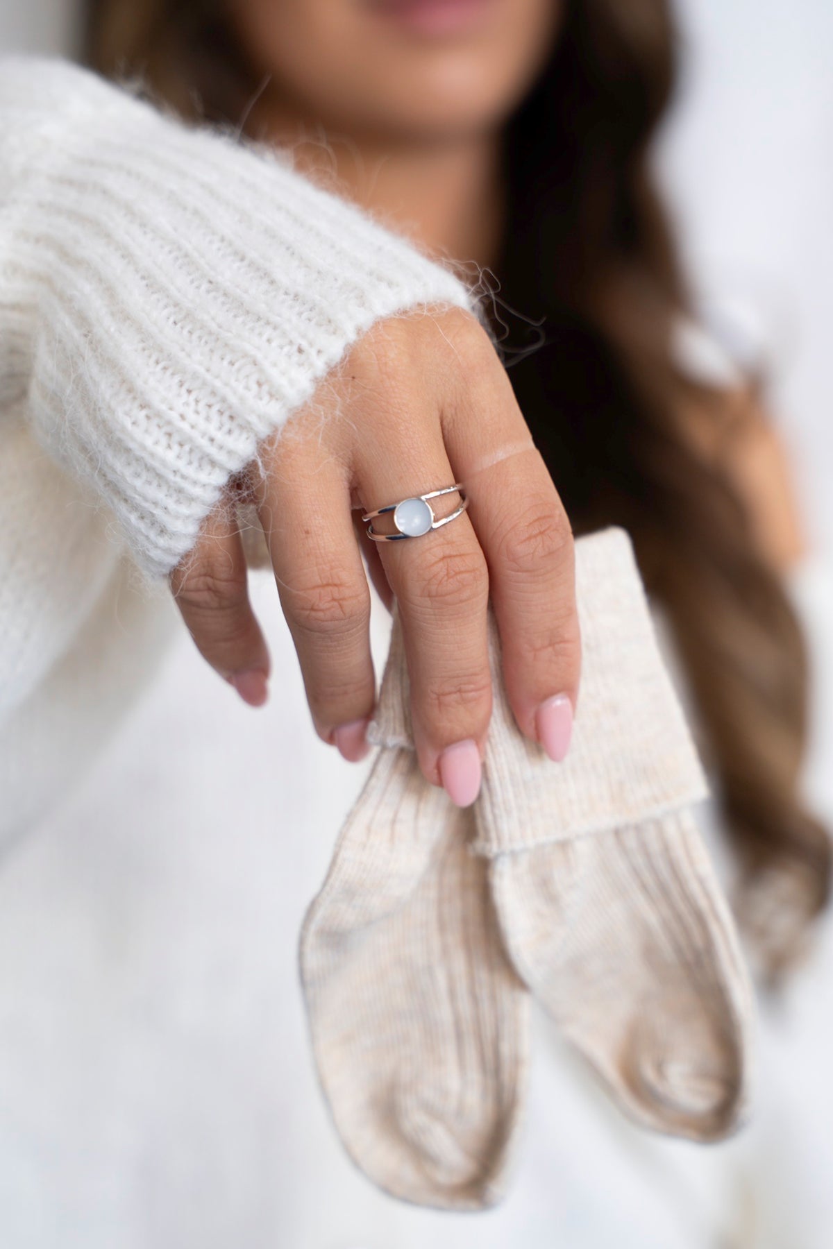 Zilveren Bea-ring met ronde moedermelksteen, gedragen door een vrouw in een witte trui die babysokjes vasthoudt.