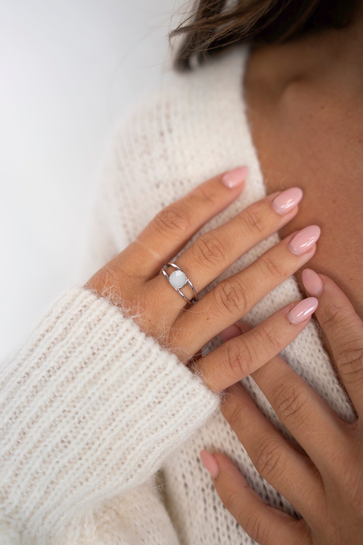Close-up van de Bea-ring van 925 zilver met ronde moedermelksteen, hand rustend op een witte gebreide trui.