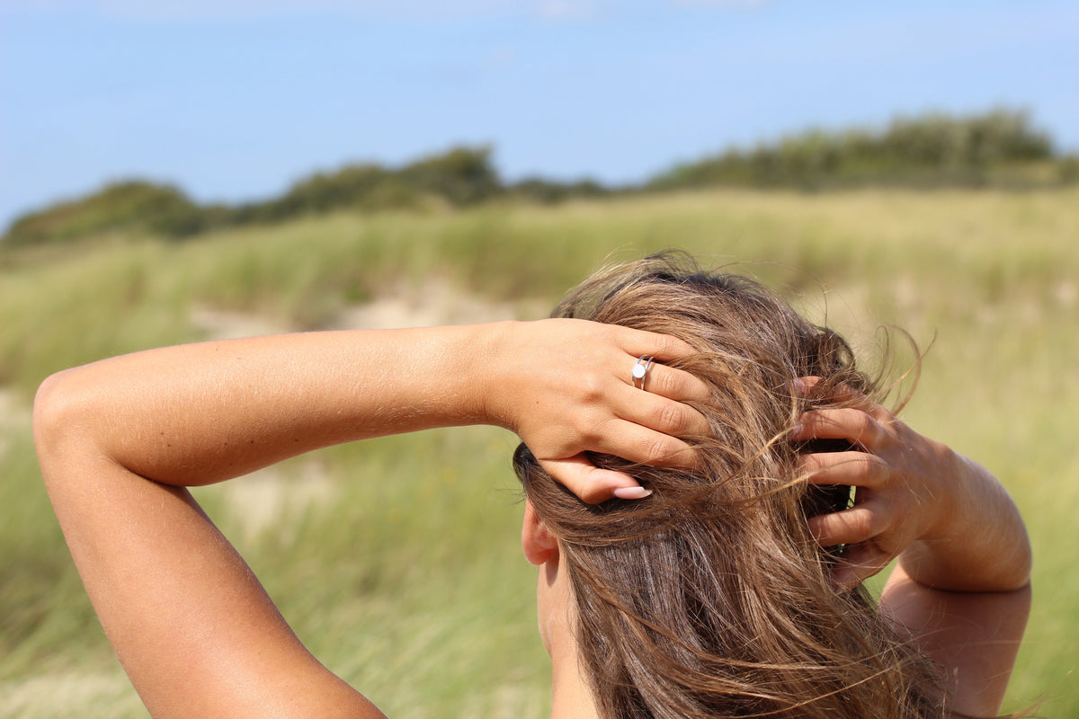 Moedermelkring van 925 zilver met een heldere steen, gedragen door een vrouw met los haar, op een zonnige locatie met gras en bomen op de achtergrond.