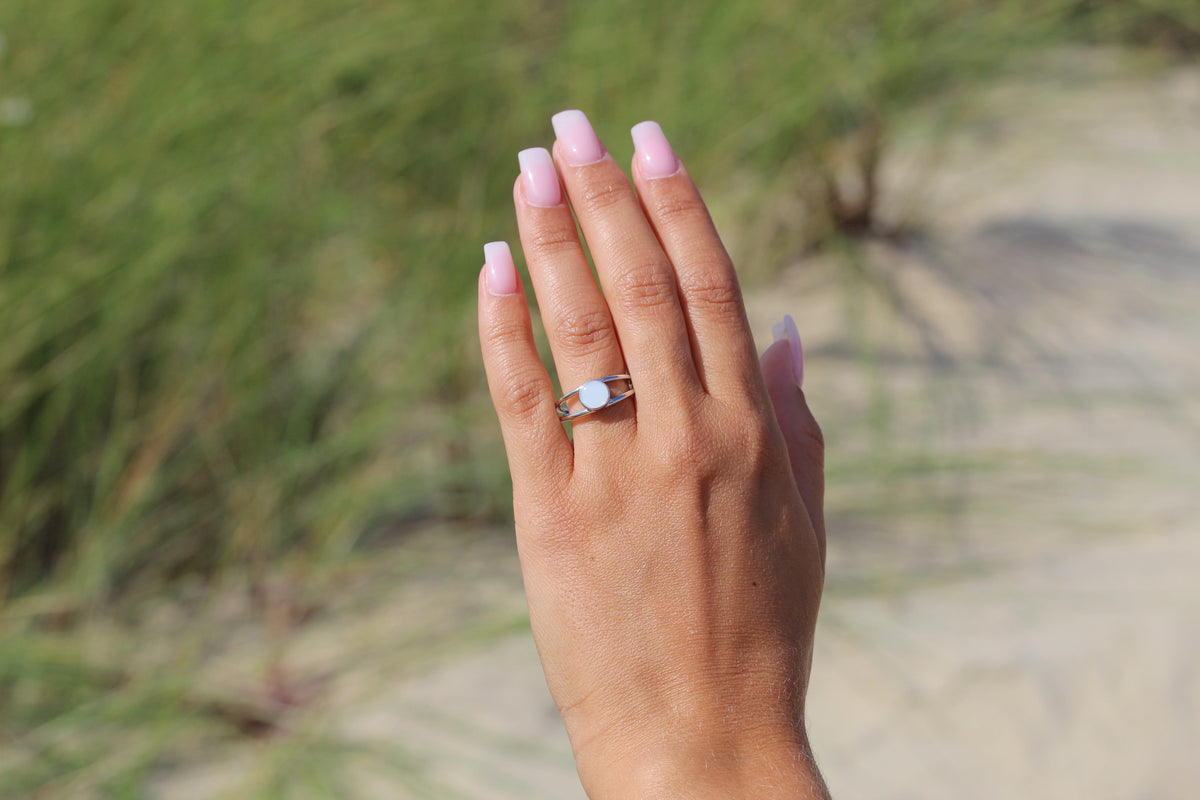 Moedermelkring van 925 zilver met een heldere harssteen, gedragen op een hand met gelakte nagels, tegen een natuurlijke achtergrond.