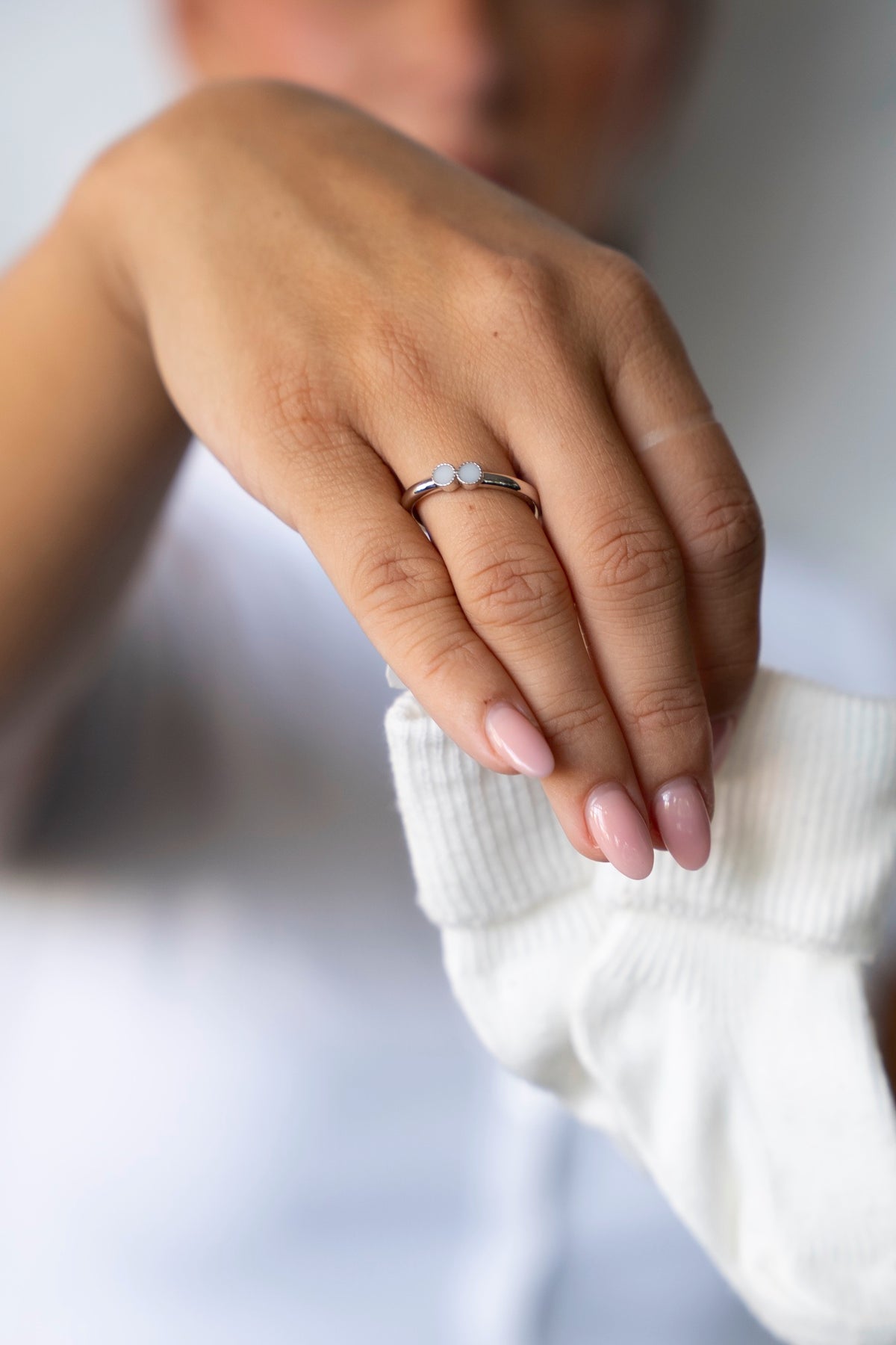 Hand met de zilveren Bo moedermelkring die een wit babysokje vasthoudt.