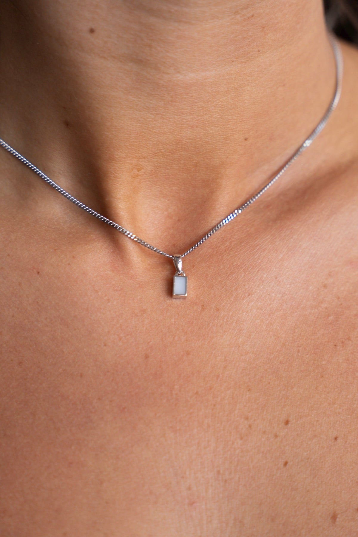 Close-up van de witgouden Britt-hanger met rechthoekige moedermelksteen om de hals.