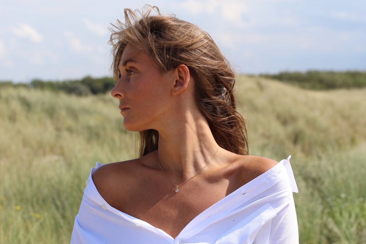Zilveren moedermelk-hanger met een ronde, transparante harssteen, gedragen door een vrouw met een open blouse, in een natuurlijke omgeving.
