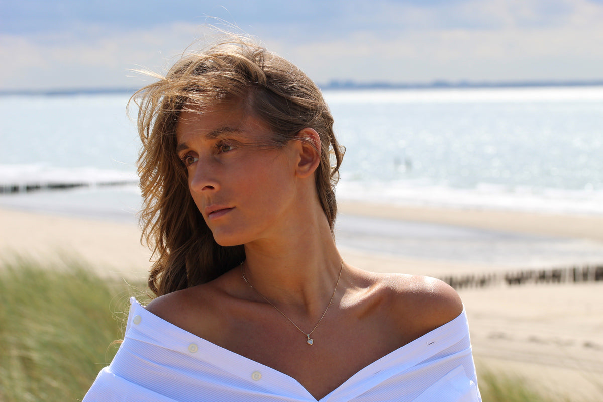 Hanger van massief witgoud met een kleine, ronde moedermelkhars en een subtiele gravure, gedragen door een vrouw met een off-shoulder blouse.