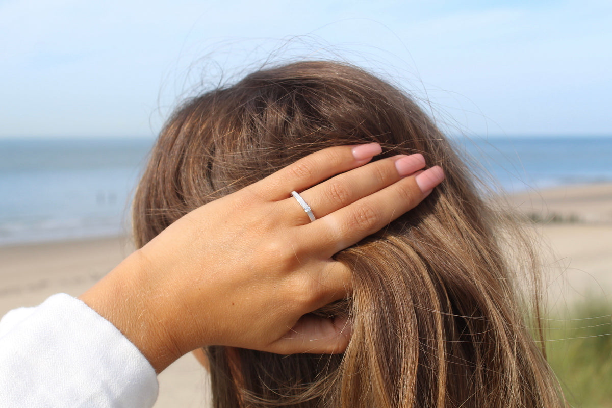 Moedermelk-ring van 925 zilver, eenvoudig ontwerp met een gladde afwerking, gedragen op een hand met lange, roze gelakte nagels.