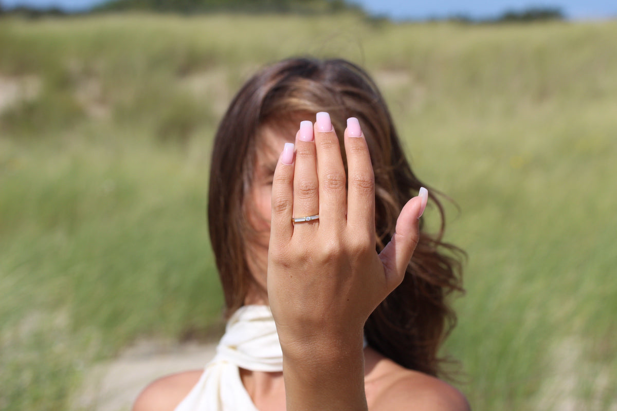 Massief geelgouden ring met een heldere zirkonia, gedragen door een vrouw met een natuurlijke achtergrond.