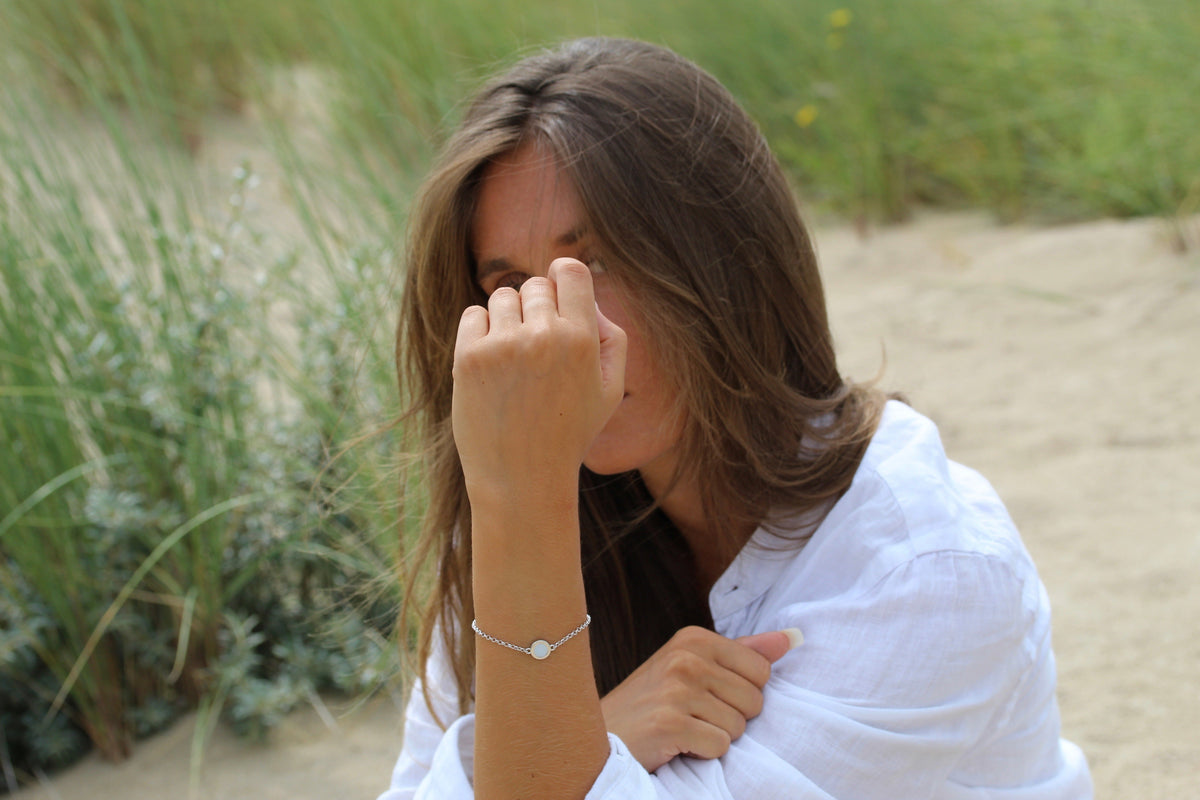 Armband van massief witgoud met een ronde schijf van moedermelkhars, gedragen door een vrouw met bruin haar in een natuurlijke omgeving.
