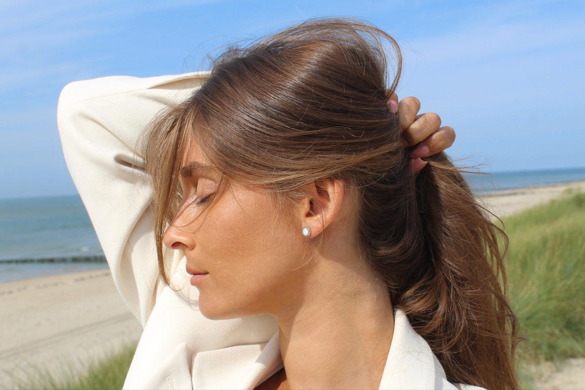 Massief gouden oorstekers met een ronde, glanzende moedermelkhars en een subtiele, elegante uitstraling, gedragen door een vrouw met een natuurlijke look.