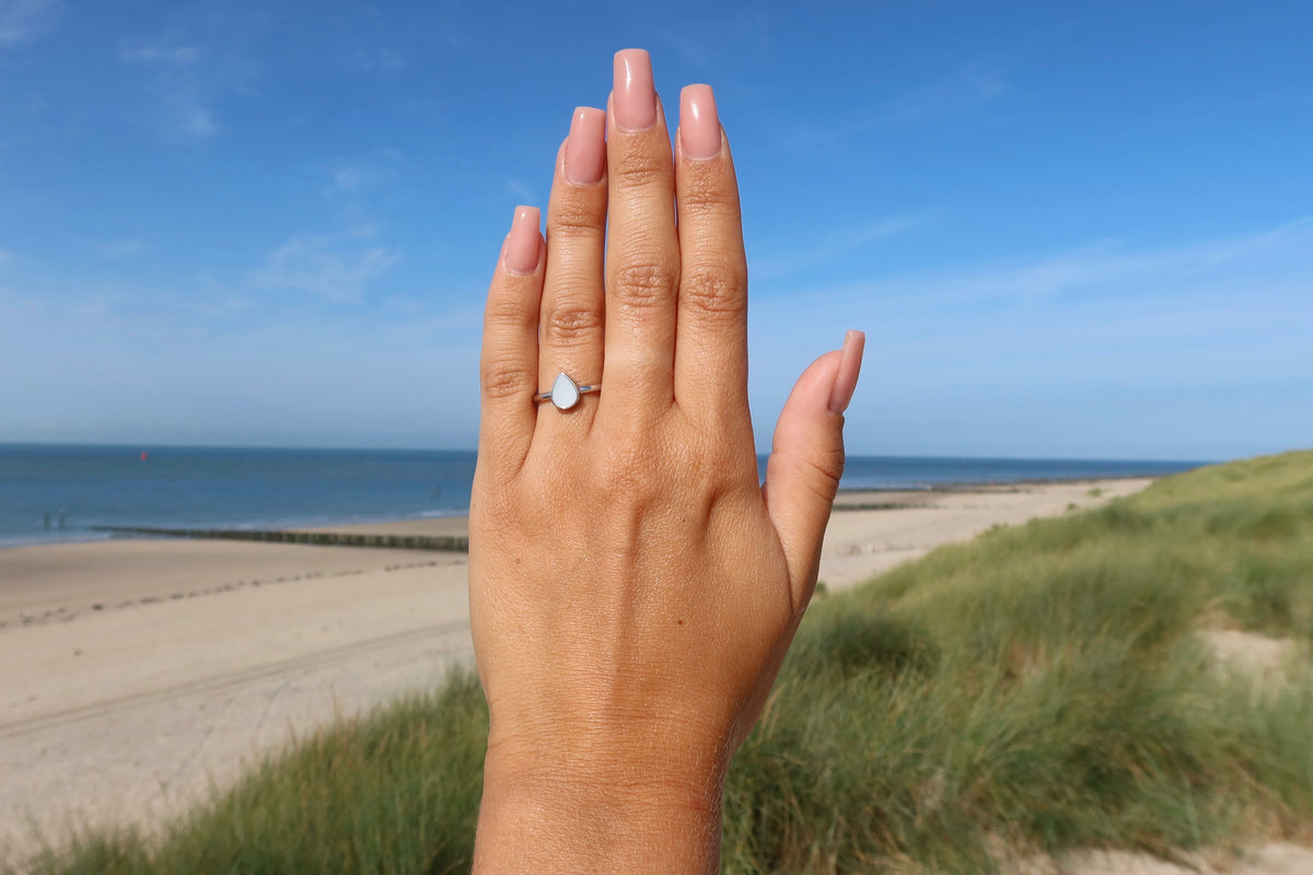 Moedermelk-ring in massief roségoud met een hartvormige steen van moedermelkhars, gedragen op een hand met een natuurlijke nagellak.