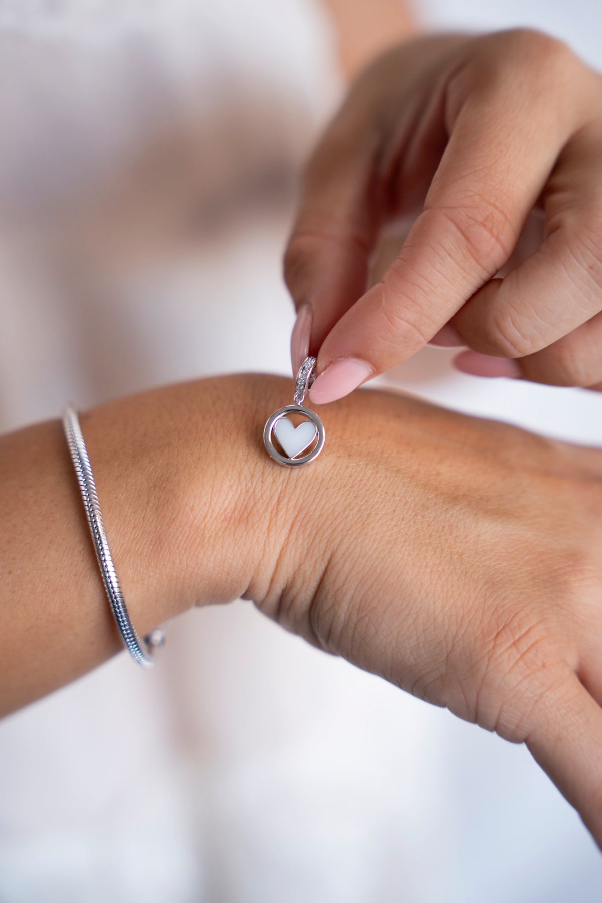 Eline moedermelkbedel van 925 zilver met hartvormige moedermelk in een rond kader, naast een zilveren armband.
