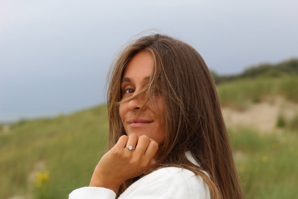 Ronde moedermelk-ring van 925 zilver met een heldere steen, gedragen door een vrouw met lang bruin haar, op een groene achtergrond.