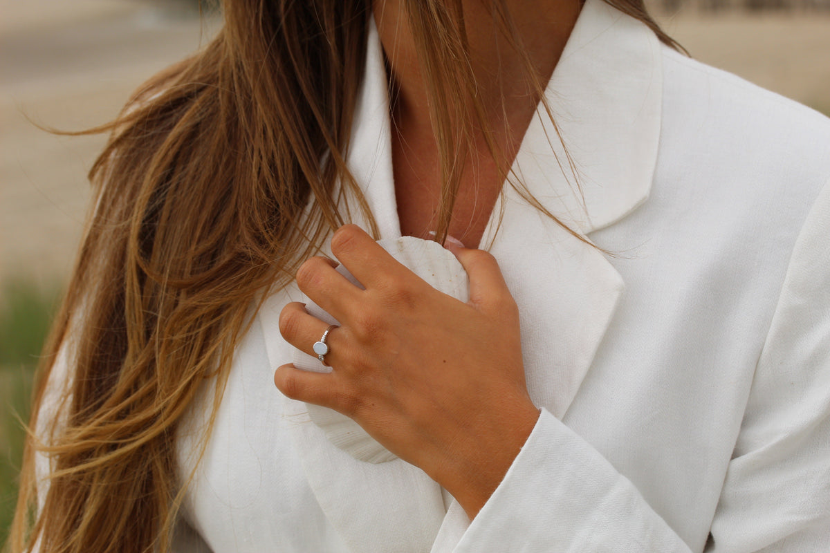 Massief roségouden ring met een ronde moedermelkhars en een sprankelende zirkonia, gedragen door een persoon met lange haren.