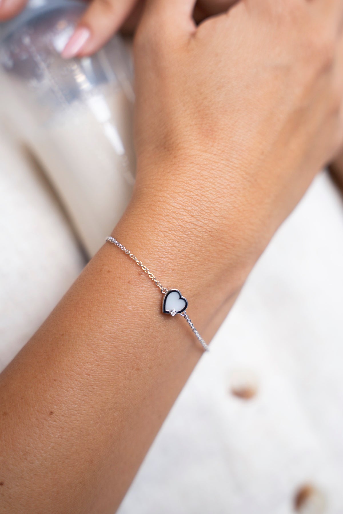 Zilveren Esmée-armband met hartvormige moedermelksteen om de pols, naast een flesje melk.