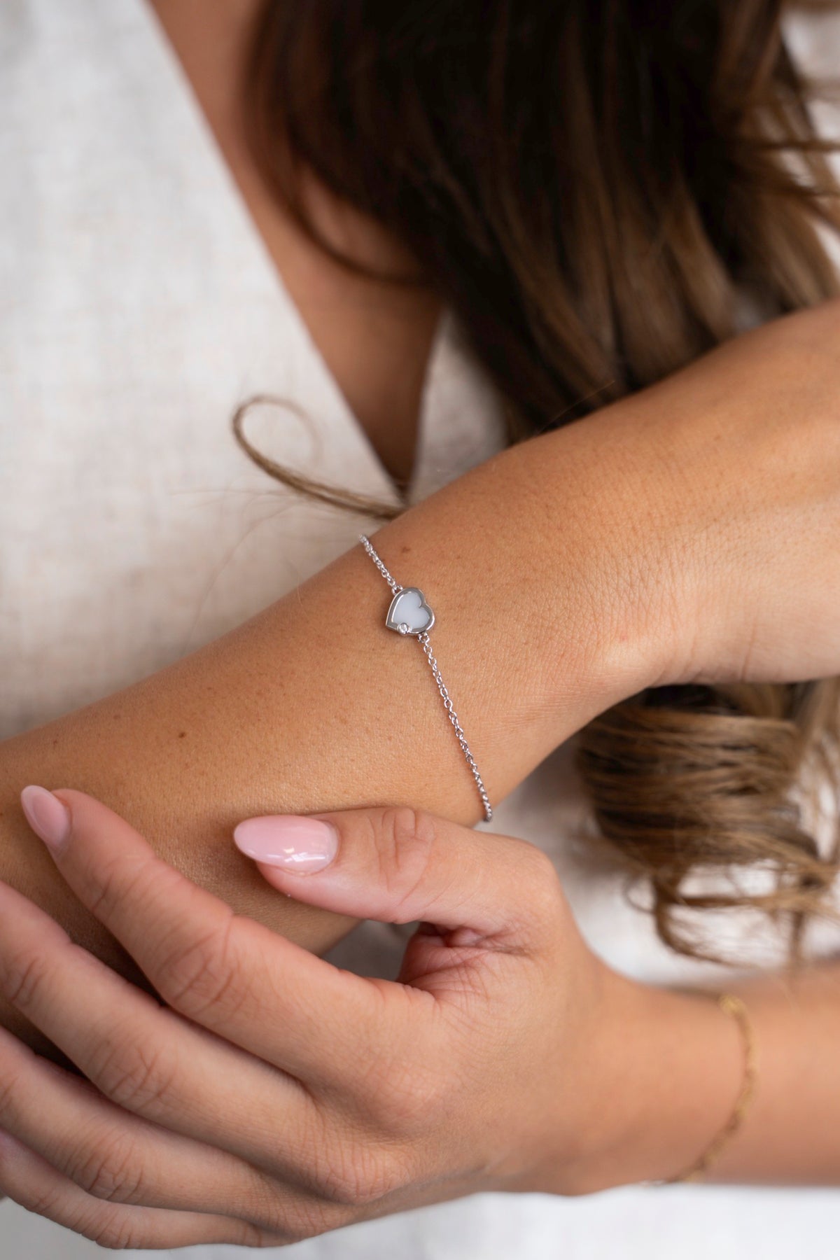Esmée-armband van 925 zilver met moedermelkhartje, gedragen om de pols tegen een linnen top.
