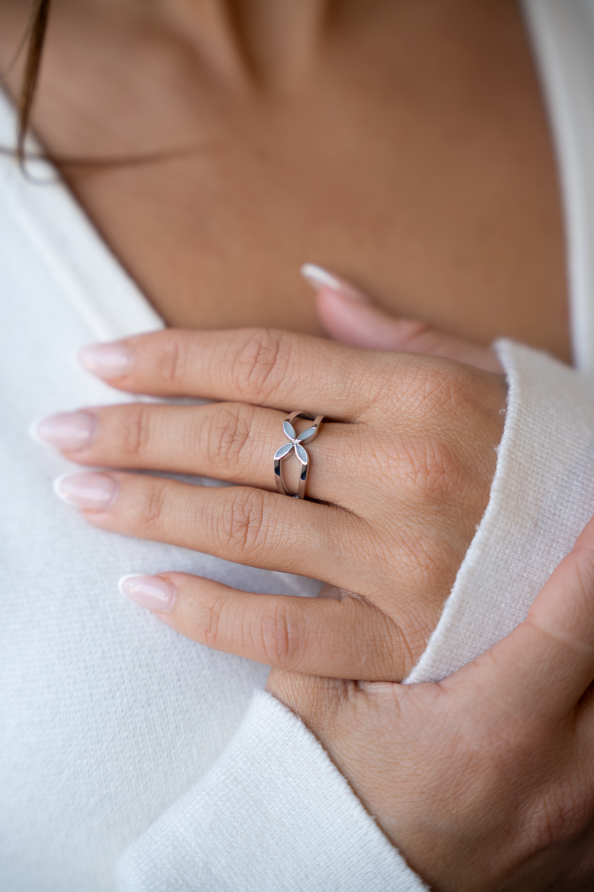 Moedermelk-ring in witgoud met een elegante, opengewerkte bloemvorm, gedragen op een hand met verzorgde nagels.