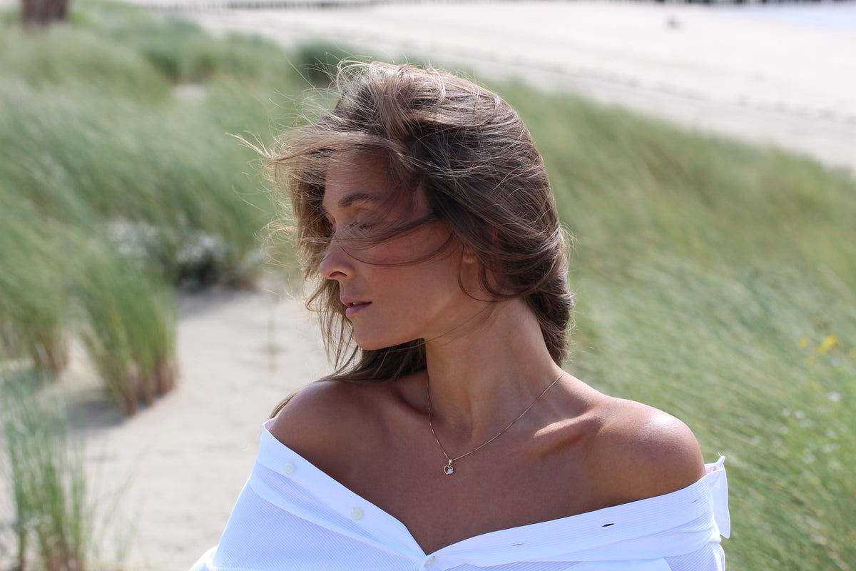 Hanger van 925 zilver met een transparant stuk moedermelkhars, gedragen door een vrouw met los haar, op een strandachtige achtergrond.
