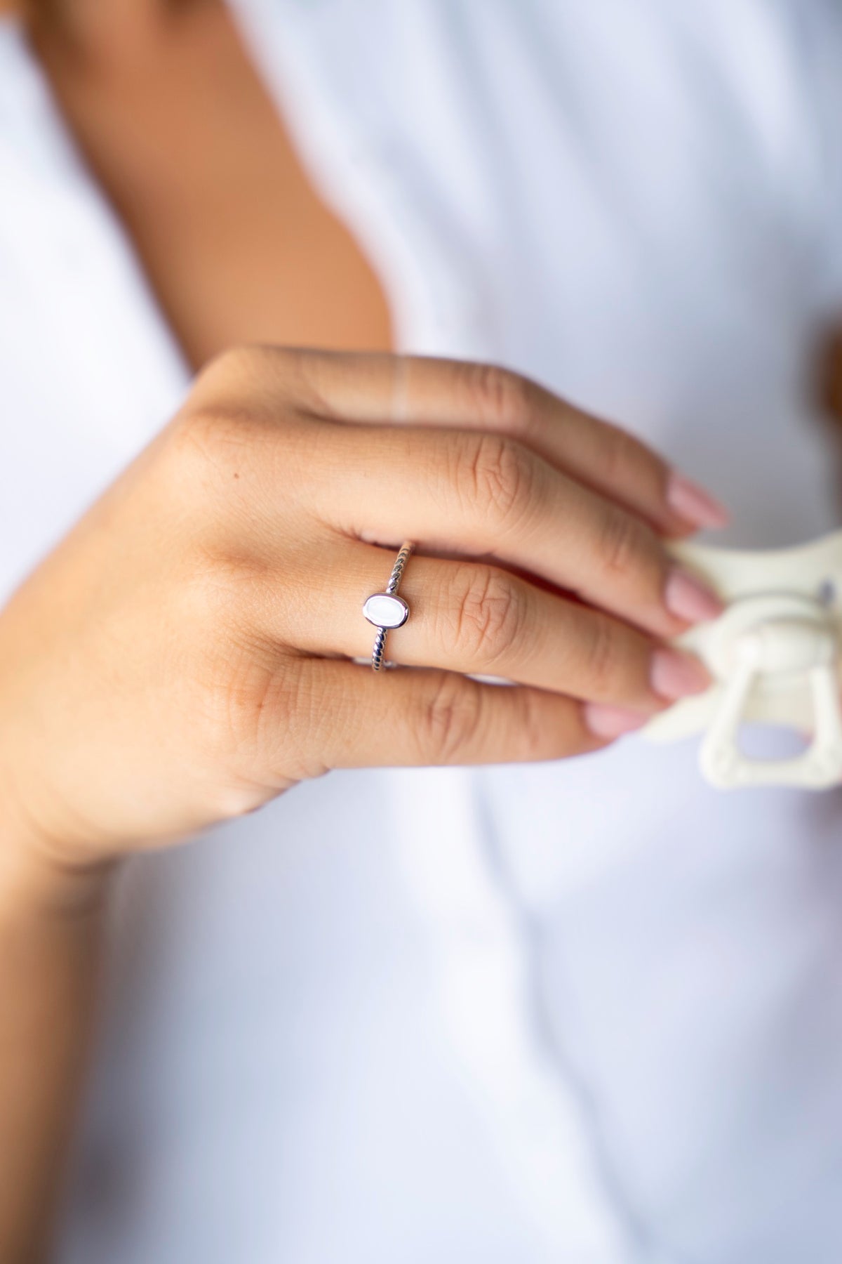 Zilveren Ilse-ring met ovale moedermelksteen en bewerkte band, met een speen in de hand.