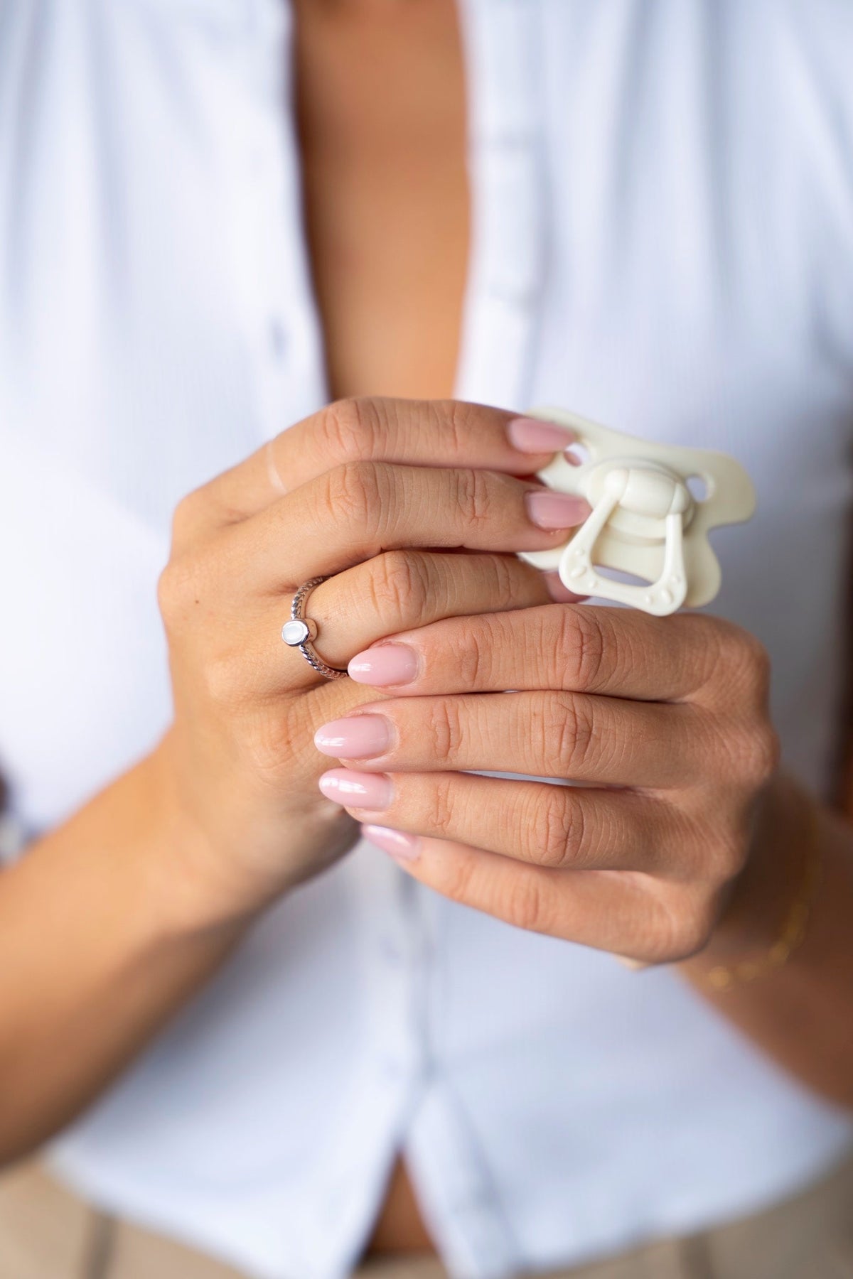 Handen houden een witte speen vast, met de Ilse moedermelkring van massief witgoud aan de vinger.