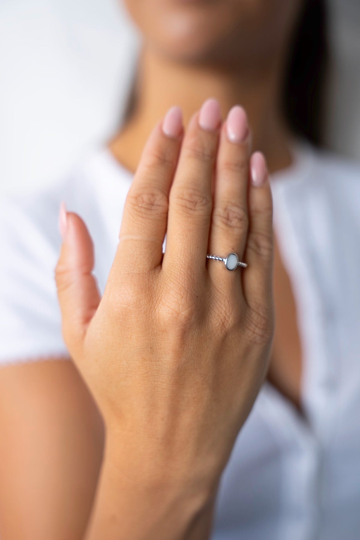 Opgeheven hand met de witgouden Ilse-ring met ovale moedermelksteen, tegen een wit shirt.