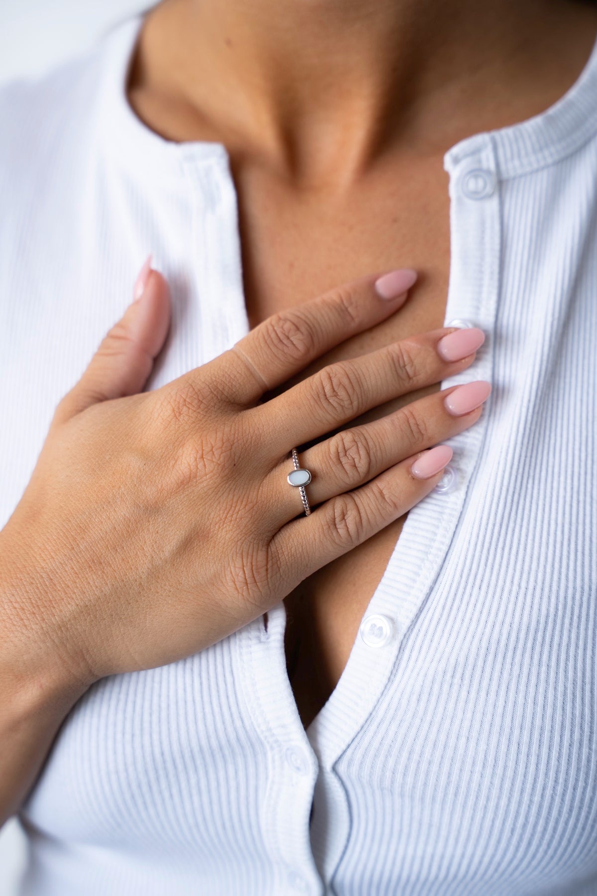 Hand op de borst met de Ilse moedermelkring van 925 zilver, gedragen bij een wit geribd vest.