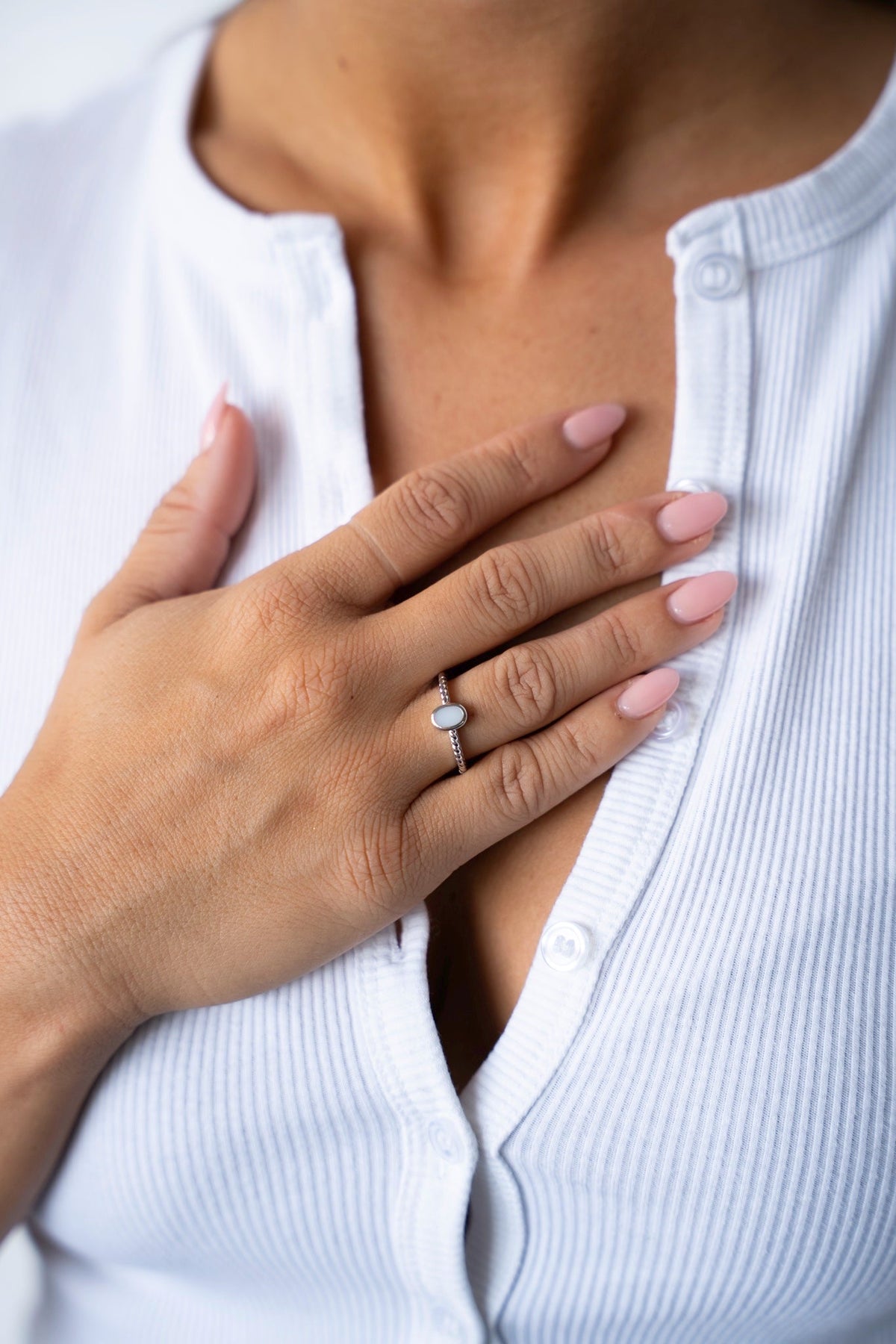 Hand op de borst met de Ilse moedermelkring van massief witgoud, gedragen bij een wit geribd vest.