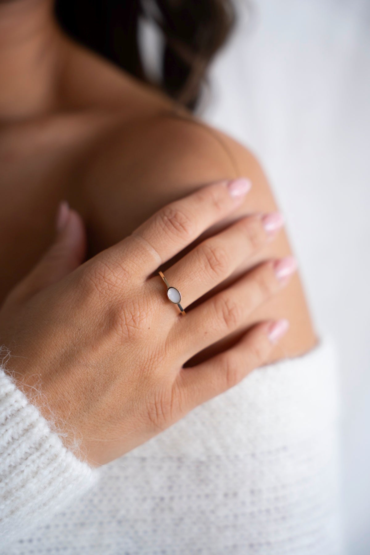 Hand op de schouder met de gouden Juna-ring met ovale moedermelksteen.