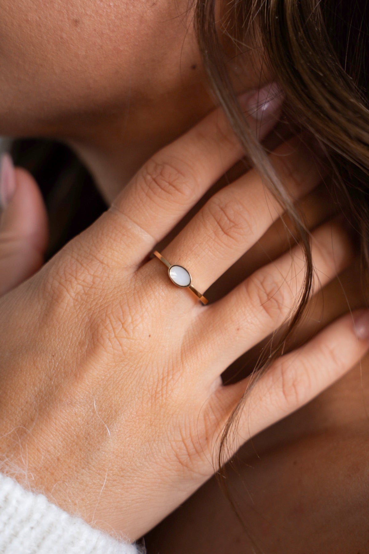 Close-up van de Juna-ring van massief geelgoud met ovale moedermelksteen, hand bij de hals.