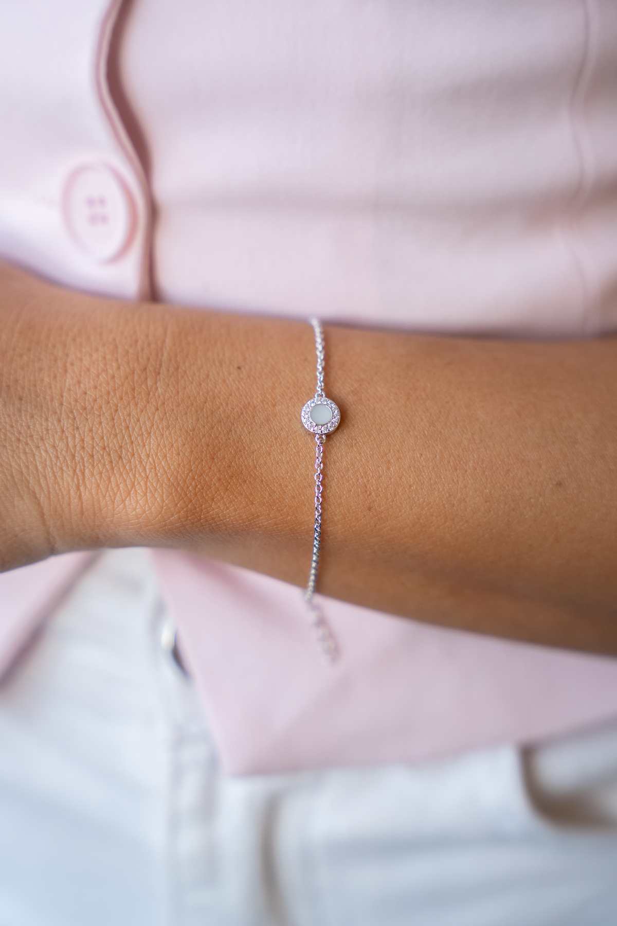 Armband van 925 zilver met een ronde schijf van moedermelkhars en een omlijsting van zirkonia, gedragen om een pols.