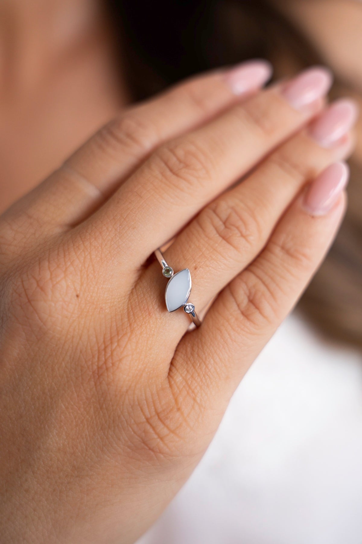 Close-up van de zilveren Lina Duo-ring: een ovale moedermelksteen tussen twee kleine geboortesteentjes, gedragen aan de hand.