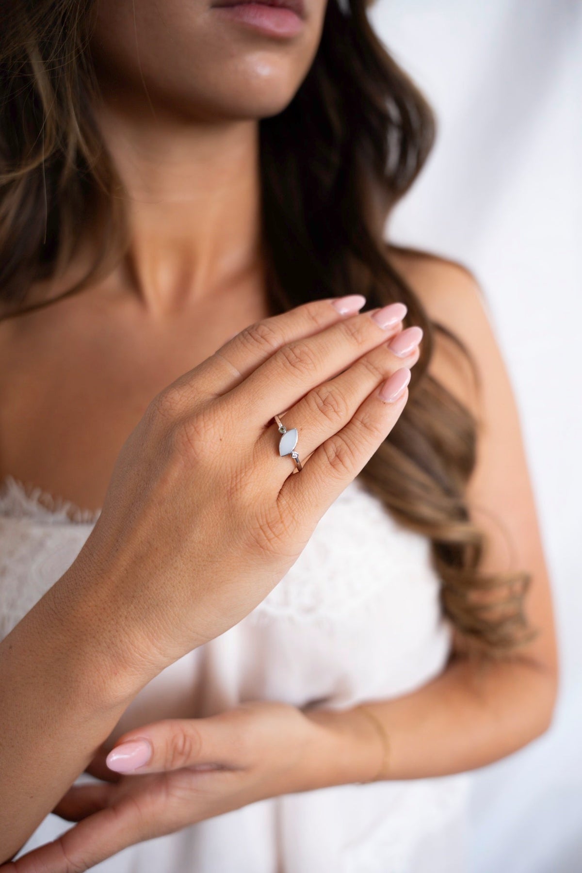 Vrouw in een witte kanten top draagt de Lina Duo moedermelkring van massief witgoud aan haar ringvinger.