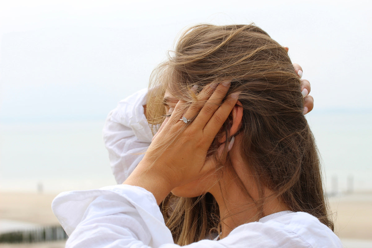 Moedermelkring van 925 zilver, met een subtiele afwerking, gedragen door een vrouw met los haar, op een strandachtergrond.