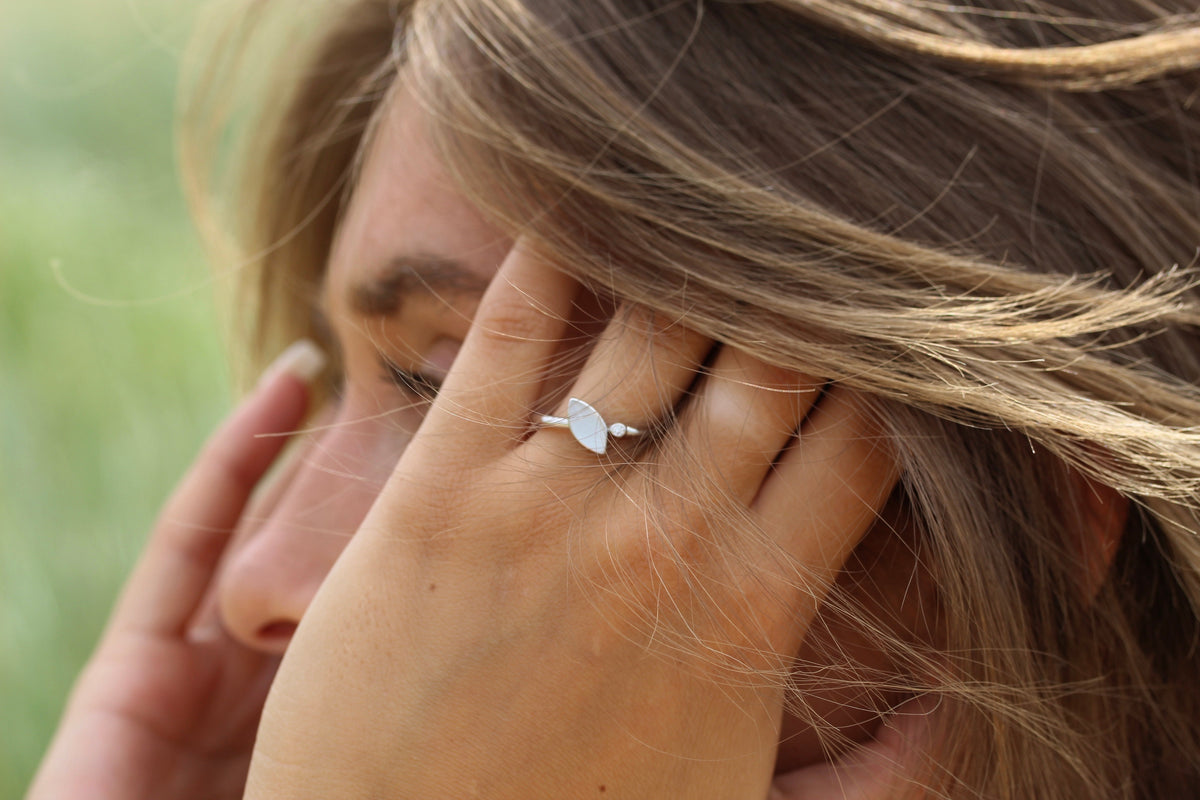 Zilveren ring met een ovale moedermelkharssteen, subtiele details en een elegante uitstraling, gedragen door een persoon.