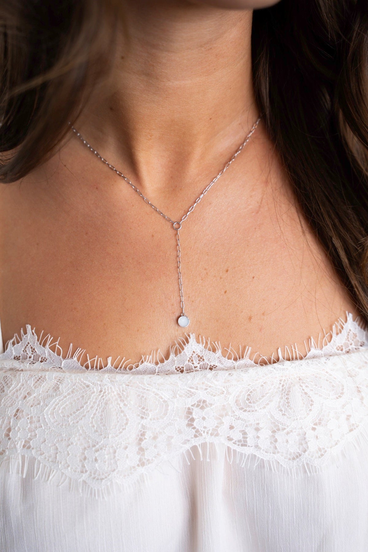 Close-up van de Norah Y-ketting van witgoud met ronde moedermelksteen op het decolleté.