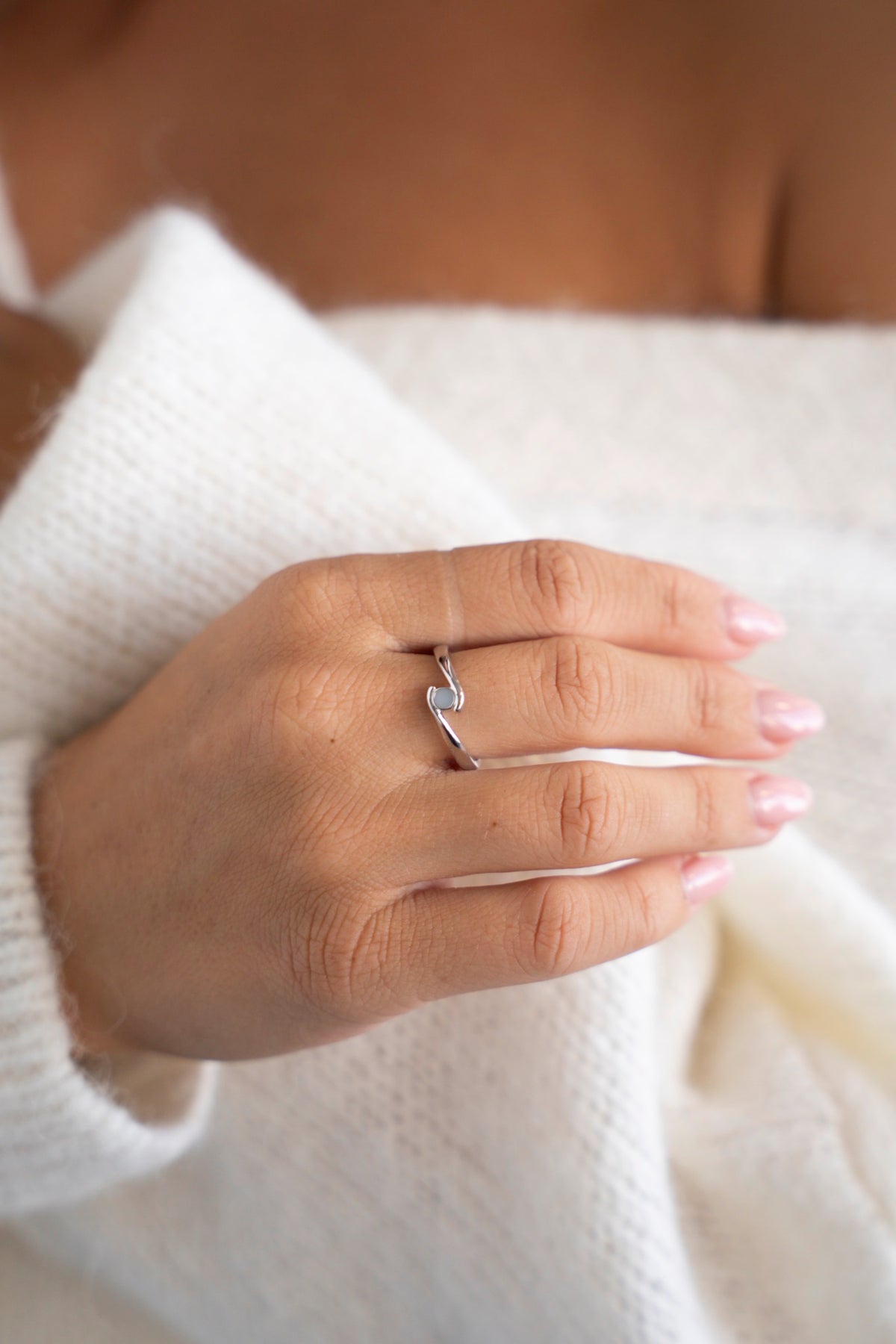 Zilveren Olivia-ring met een kleine moedermelksteen, hand op een witte trui.