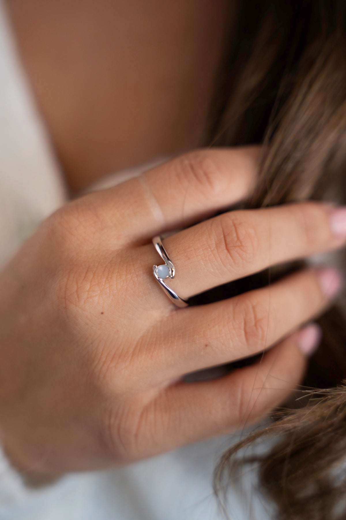 Olivia moedermelkring van 925 zilver aan een hand in het lange, golvende haar.