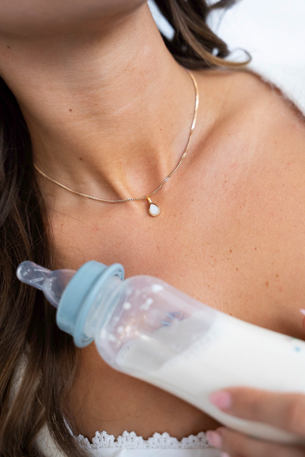 Gouden Pure Drop-hanger met druppelvormige moedermelksteen om de hals, naast een babyflesje met melk.
