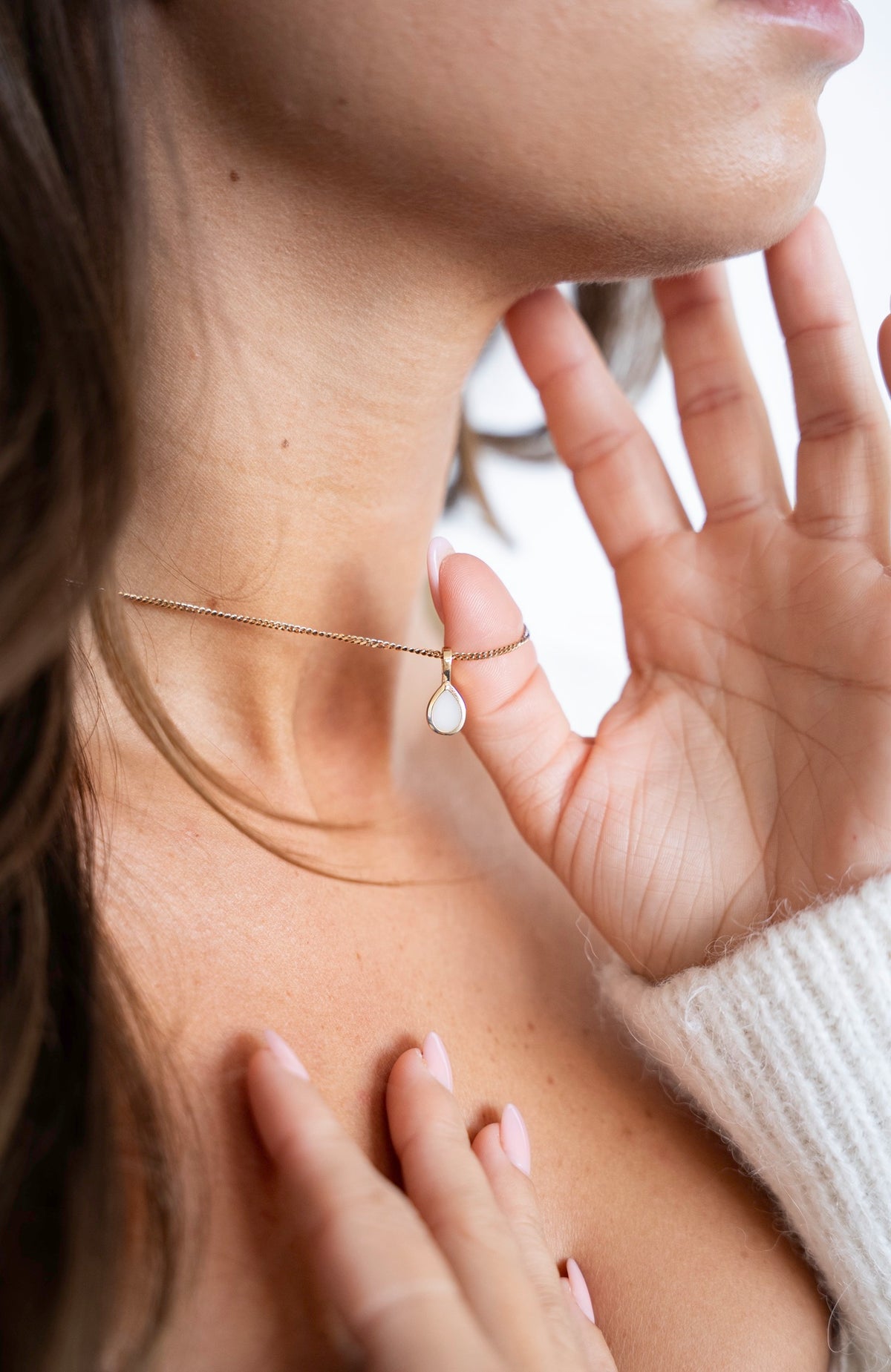 Pure Drop-hanger van massief goud met druppelvormige moedermelksteen, hand bij de hals.