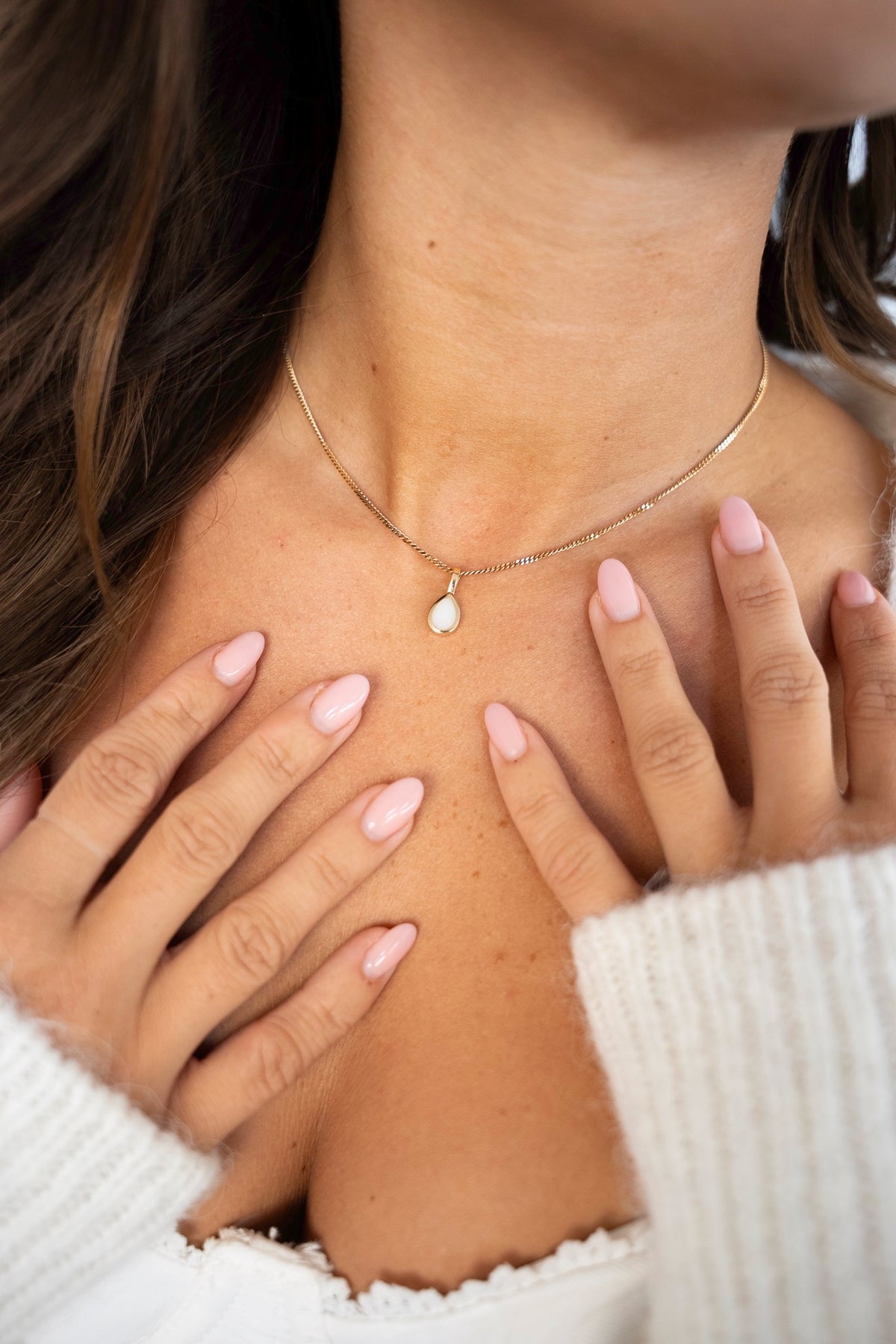 Close-up van de gouden Pure Drop-hanger met witte moedermelkdruppel, handen op de borst.