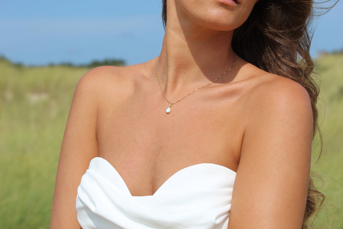 Hanger van massief roségoud met een druppelvormige moedermelkhars, gedragen door een vrouw in een strapless witte top, met een natuurlijke achtergrond.