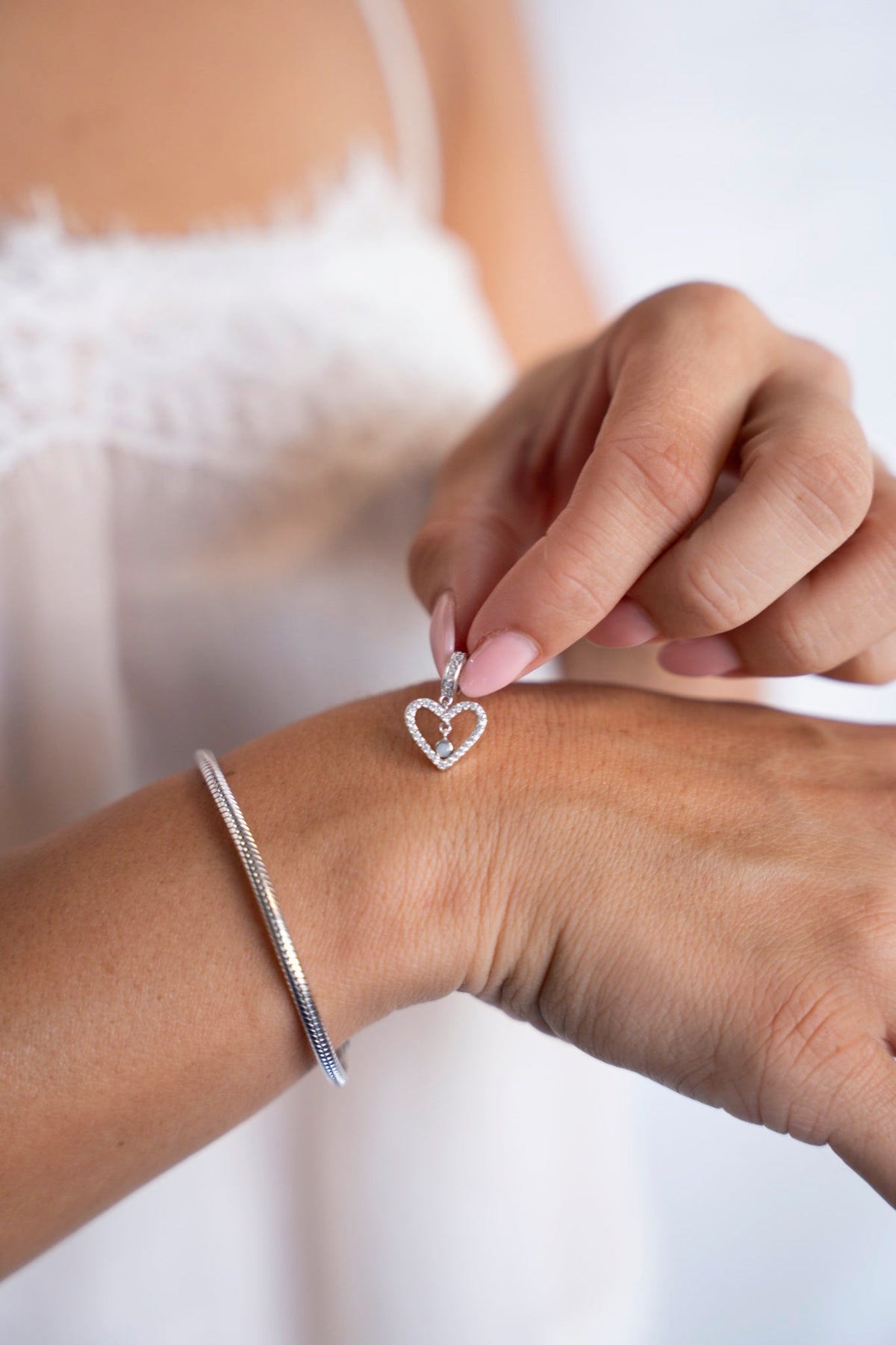 Sophie hartjesbedel van witgoud met moedermelk, naast een armband om de pols.