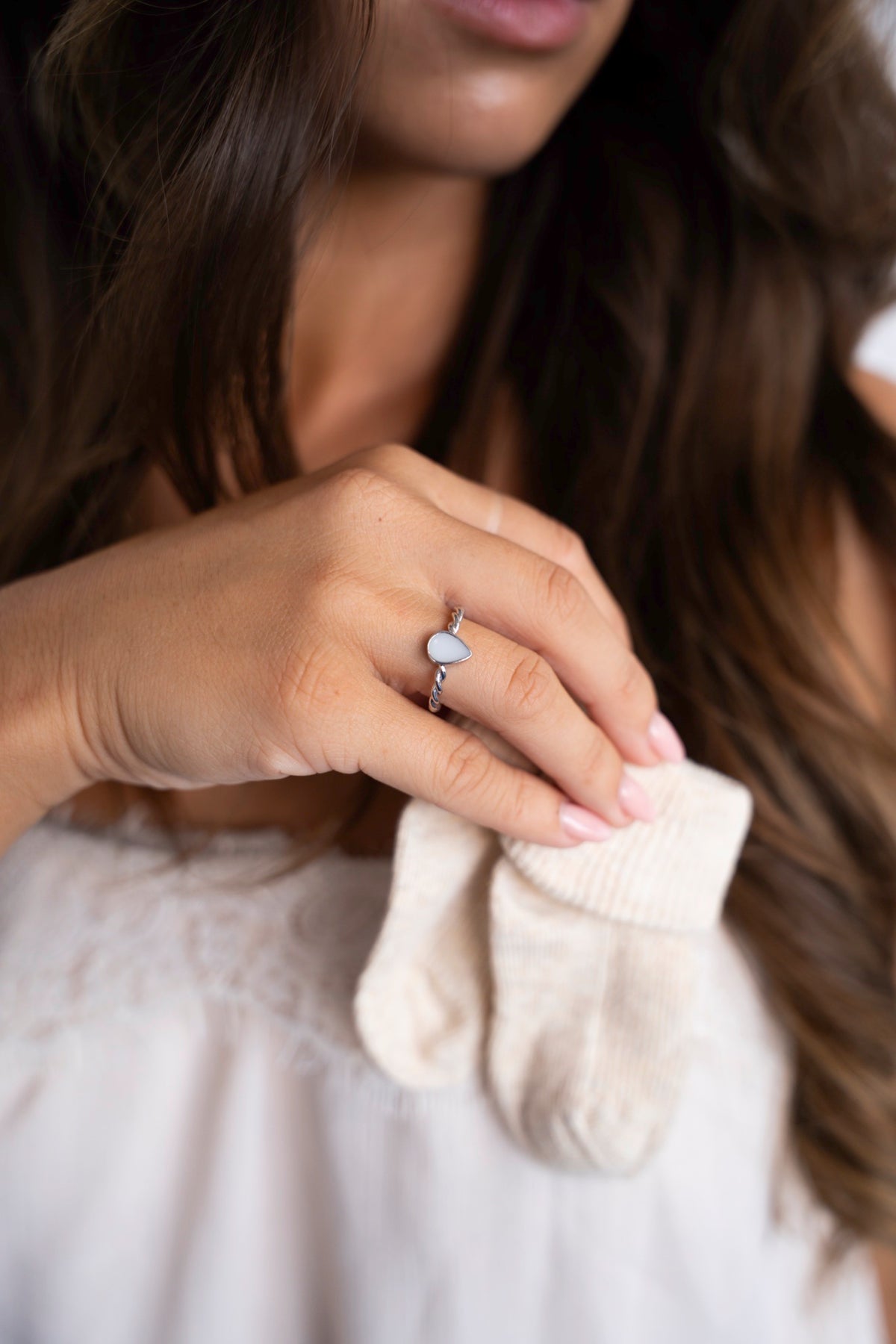 Zilveren Turning Droplet-ring met druppelvormige moedermelksteen, hand houdt babysokjes vast.